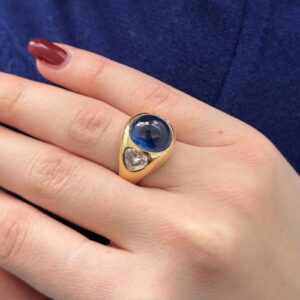 Foto gioiello indossata: anello oro giallo a fascia bombata con zaffiro centrale e diamanti a forma di cuore laterali